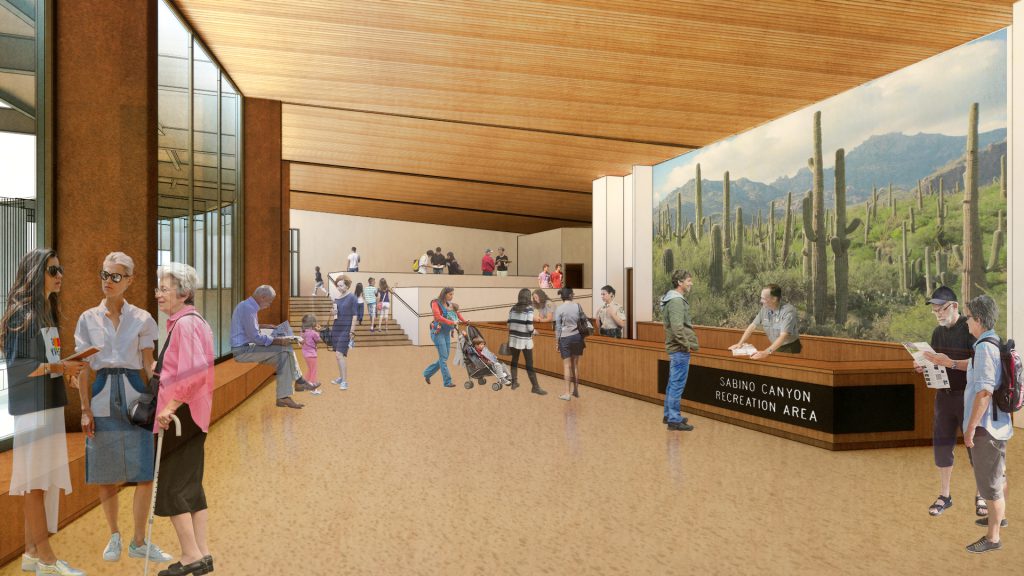 Bright visitor center interior with high ceiling, large windows. People present, welcoming atmosphere.